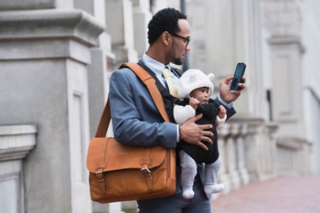 Businessman with son in baby carrier texting on cell phone