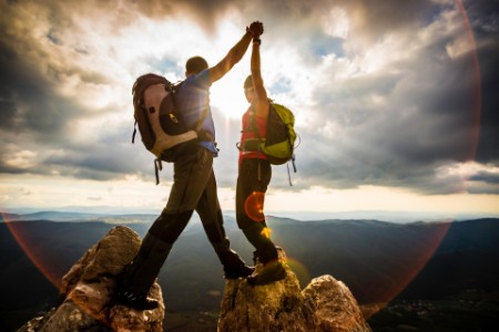 Couple on top of a mountain shaking raised hands