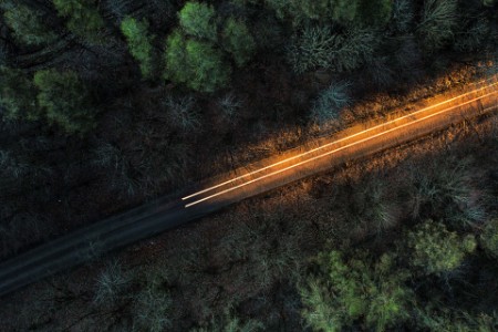 A long exposure from a drone shows a light trail of a single car on a road through the forest