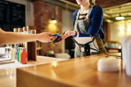 Female Barista Taking Smartphone Contactless Payment From Coffee Shop Customer