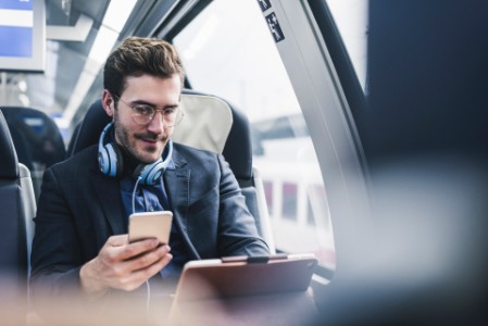 Businessman in train with cell phone, headphones and tablet