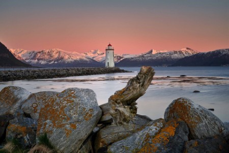 Lighthouse in pink sunset with mountains and ocean