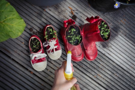 Girl spraying water onto cress plants in repurposed old shoes