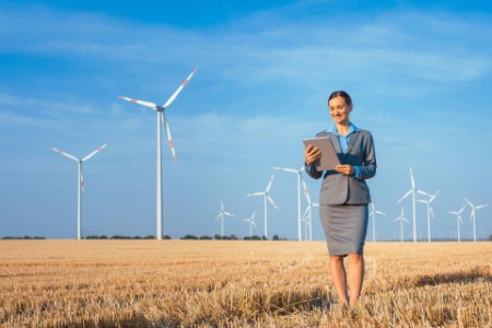 Woman checking tablet while walking in field with wind mills