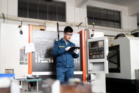 Engineer using computer in front of CNC machine tool