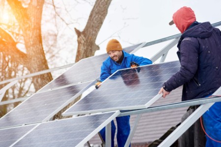 Technicians mounting blue solar modules on roof of modern house