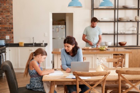 Mother Helps Daughter With Homework As Father Makes Meal