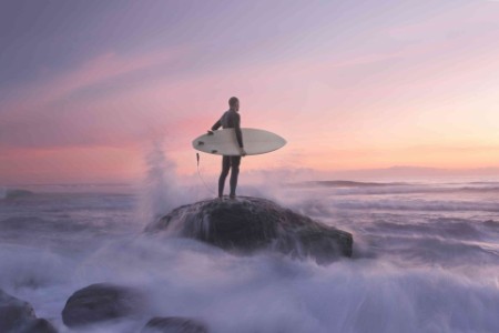 Man holding a surf board standing on a rock