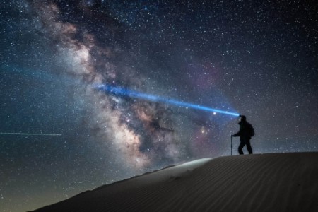Man standing on sand dune with headlamp on and milky way as backdrop