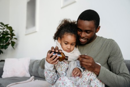 Smiling man giving medicine to daughter on sofa