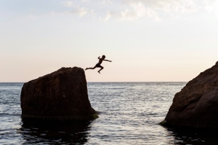 Boy jumping off the rock into the water