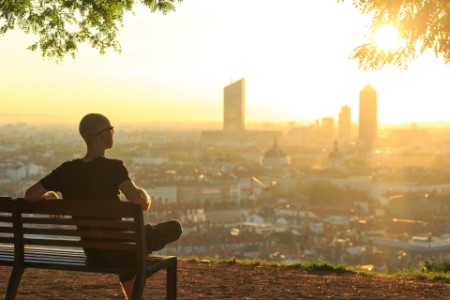 Man sitting on a bench watching the sun set over a city 