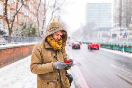 Photo of a man using his phone in a city when it is snowing
