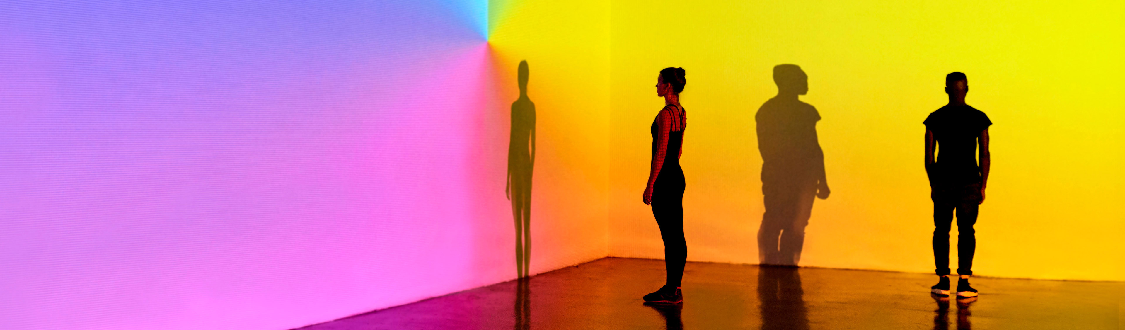 Man and woman standing in a gallery space with colourful walls background