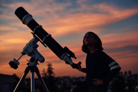 Girl with astronomical telescope under twilight sky