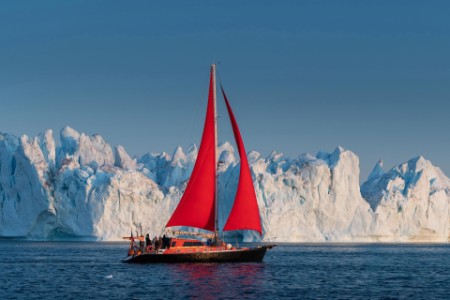 Sailboat with red sails in front of large icebergs