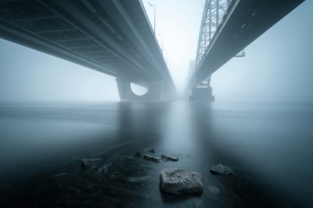Two parallel bridges over foggy river with stones in the water