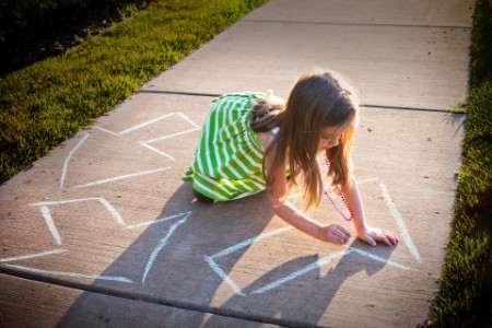 A young girl writing a recycling symbol on the sidewalk