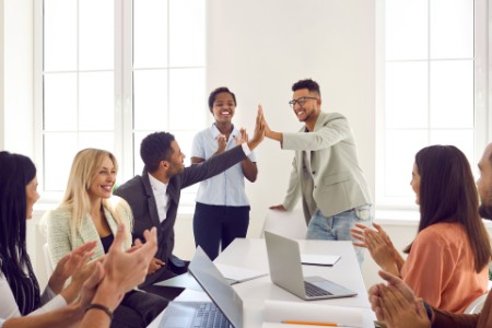 Happy young man gives high five to colleague while diverse business team is applauding