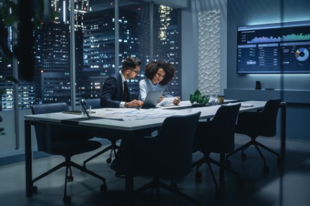 Businesspeople in Modern Office: Business Meeting of Two Managers. CEO and Operations Director Talk, Discuss, Brainstorm Corporate Strategy, Implementing Marketing and Financial Plans. Night Shift.