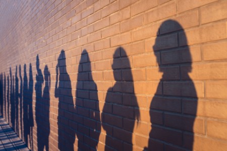 People crowd shadows lined up against a red brick wall