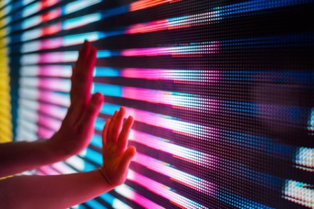 Close up of a mother and kid's hand touching illuminated and multi-coloured LED display screen