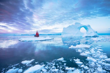 Sailboat with red sails cruising among icebergs