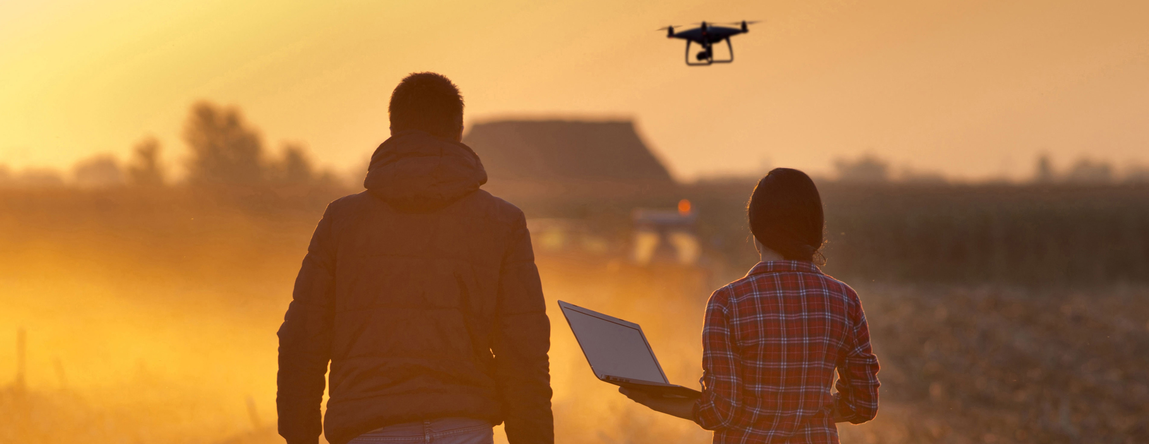 Hombre y mujer caminando en el campo, manejando un dron con la computadora portátil