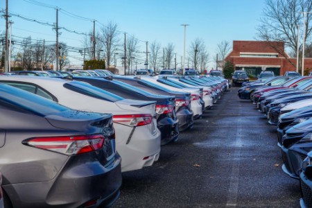View of the back of a row of various colored new cars in a parking lot