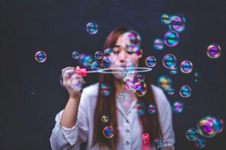 ey-woman-blowing-bubbles-against-dark-wall