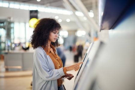Une femme qui touche l’écran tactile d’un distributeur bancaire dans un aéroport