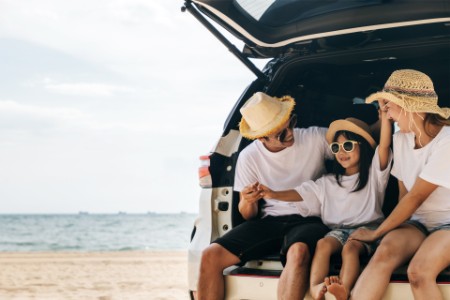 Une famille de trois personnes assise sur le coffre d’une voiture sur la plage