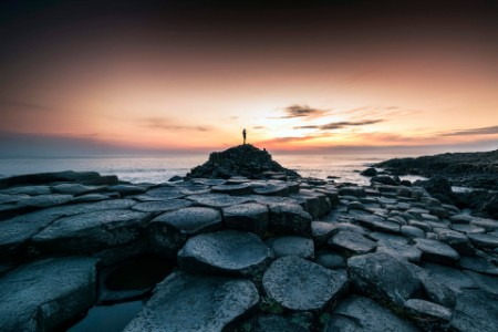 Personne sur rivage rocheux au coucher de soleil.