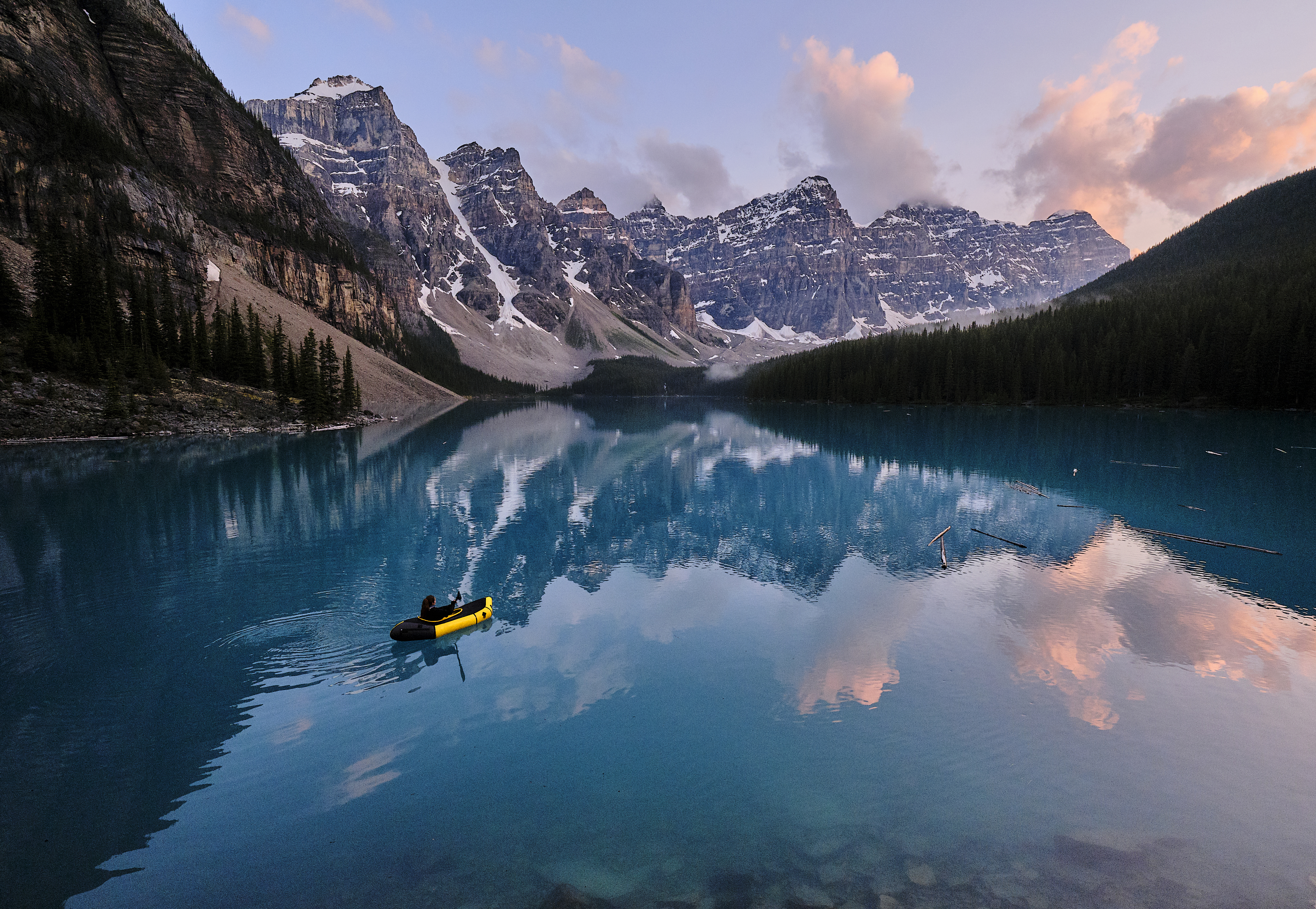Young woman kayaks across mountain lake at sunrise
