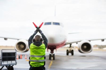 Ground Worker Signaling To Airplane On Runway