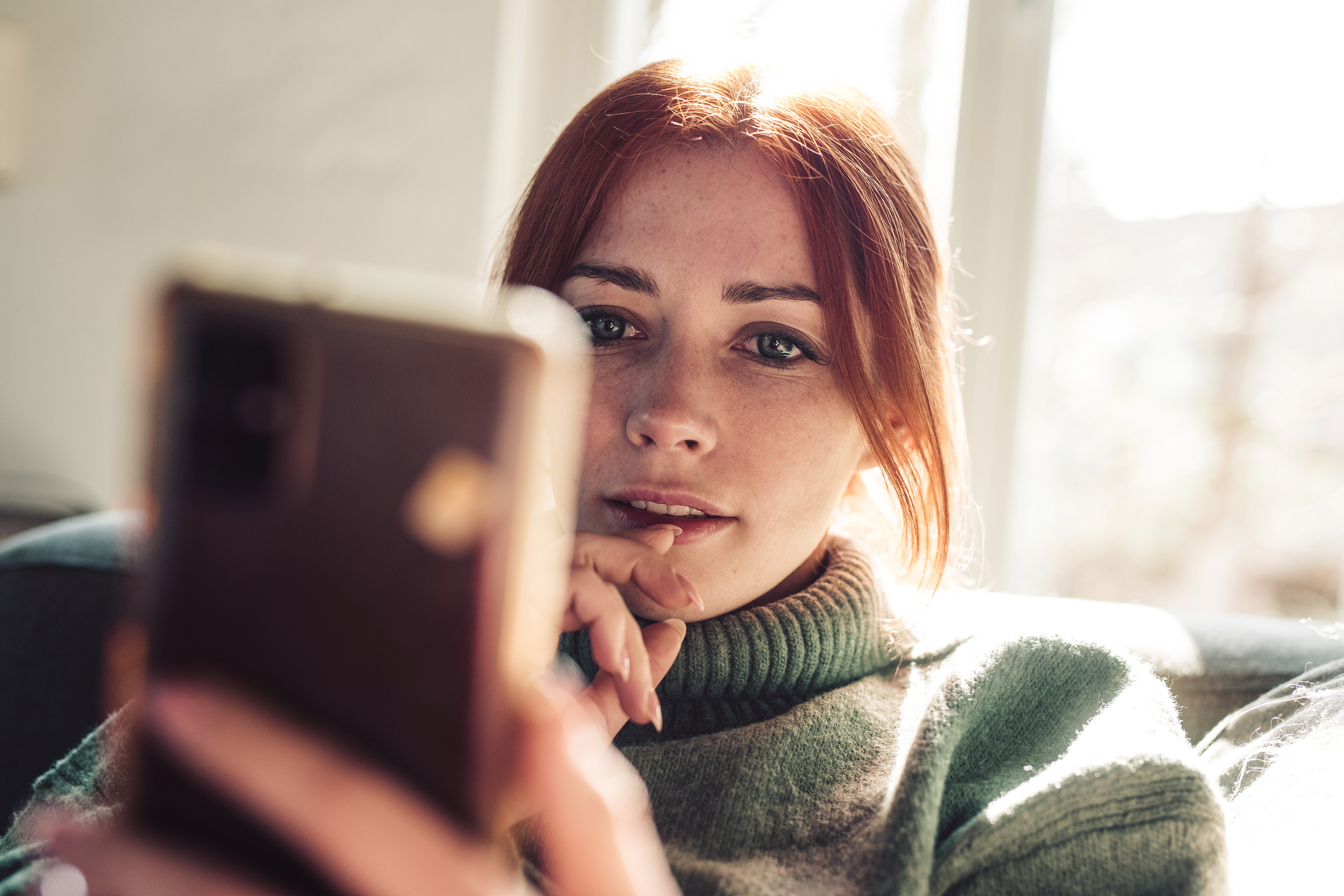 Vrouw met rood haar kijkt naar het scherm van haar mobiele telefoon.