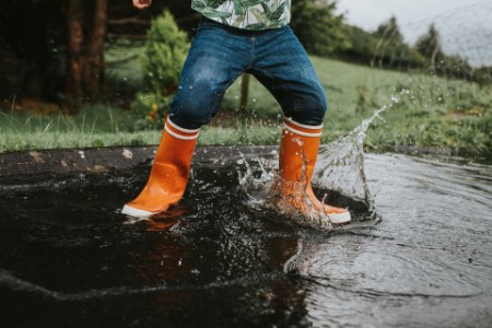 Kind in oranje regenlaarzen springt in een diepe plas