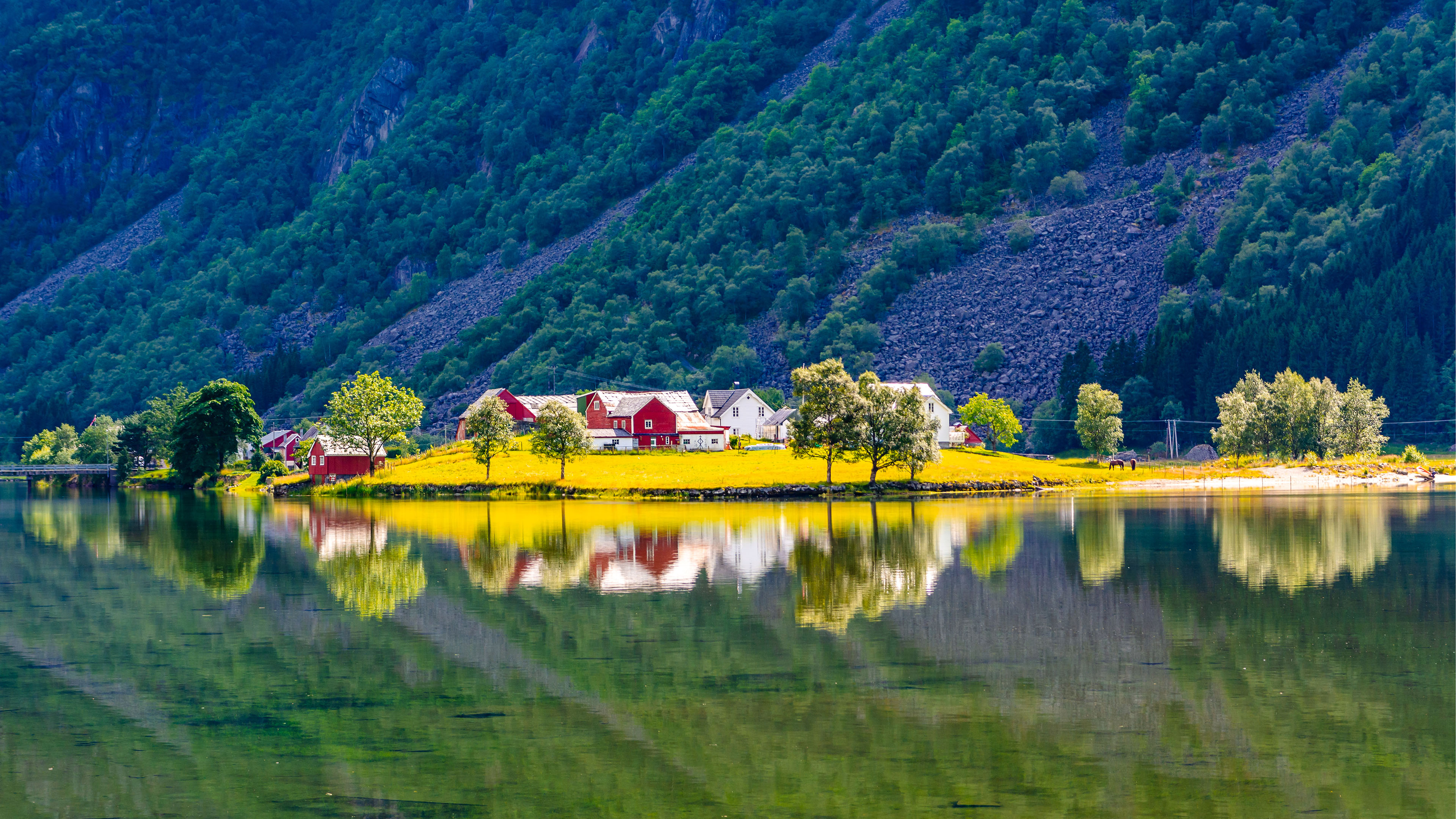 Bilde av gårdstun som speiler seg i en innsjø med fjell i bakgrunnen