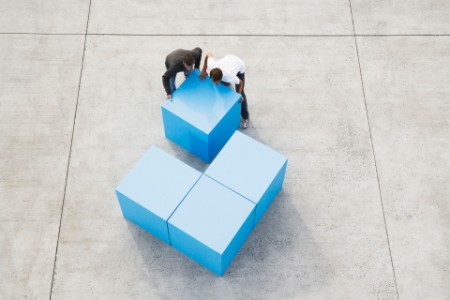 Kék kockákból álló nagy kocka, amelyet két férfi rak össze