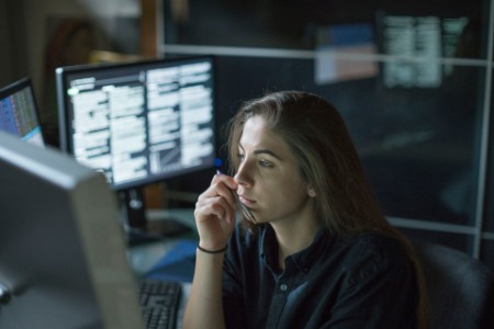 Kvinne sittende ved skrivebordet omgitt av skjermer som viser data