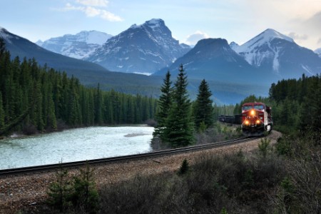 Bilde av kjørende tog omringet av vakker natur med fjell, skog og vann
