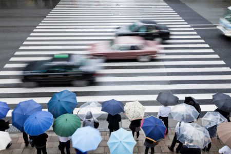 Pedestrians Waiting To Cross A Busy Road On A Rainy Day