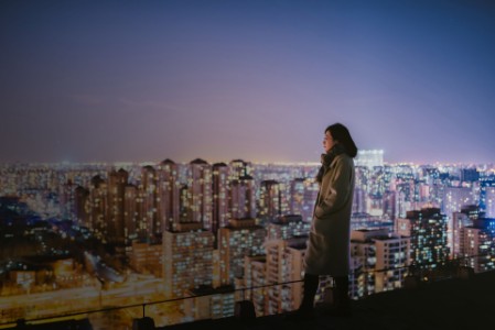 mulher no topo de um prédio olhando uma grande cidade iluminada.