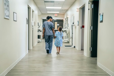 enfermeira caminha e conversa com uma criança em um corredor de um hospital