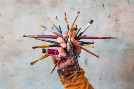 Person holding paint tubes and brushes