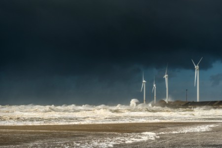 Four wind turbines amidst fierce storm waves and clouds at coast
