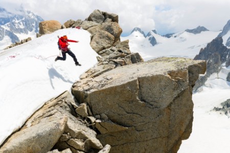 En bergsklättrare hoppar mellan bergstoppar i ett snötäckt bergslandskap