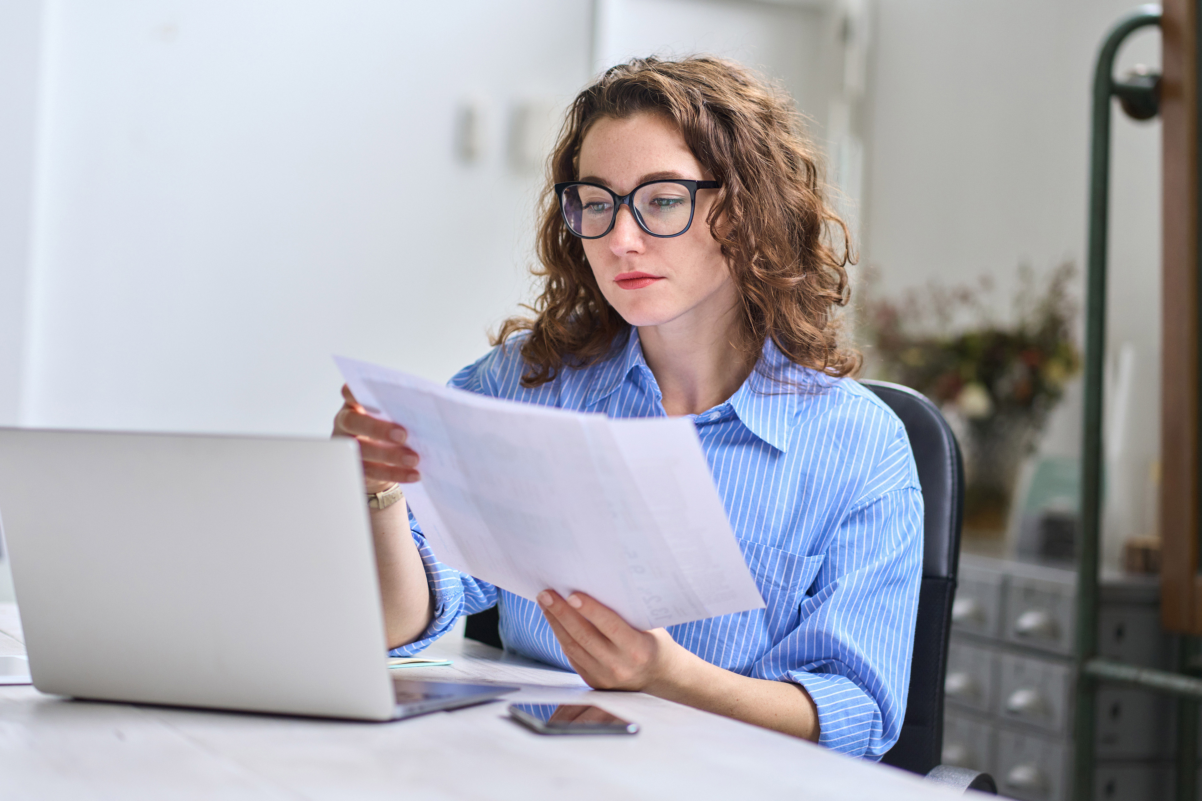 Young business woman manager holding documents working in office with laptop