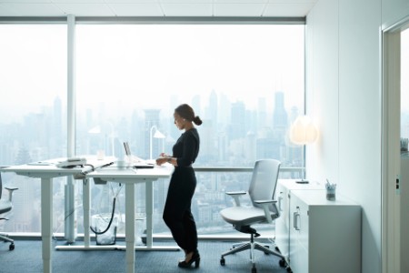 Bild på Kvinna står vid skrivbord vid stort fönster
