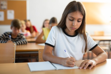 Sınıftaki masasında yazı yazan kız öğrenci
